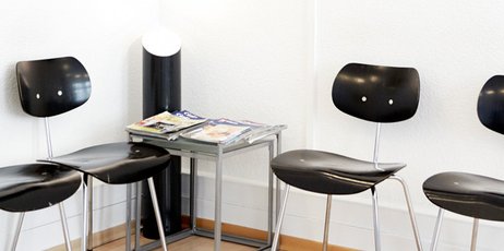Ein weißer Raum mit vier Stühlen und einem Tisch mit Magazinen drauf.