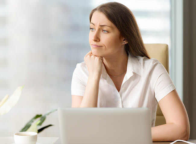 Eine Frau sitzt vor ihrem Computer und schaut enttäuscht zur Seite.