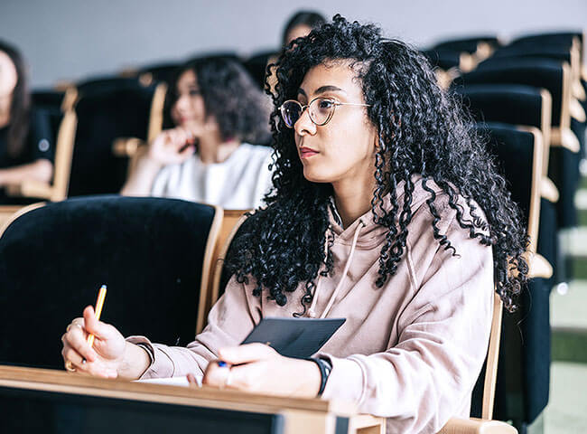 Eine junge Studentin sitzt im Hörsaal und macht sich Notizen. 