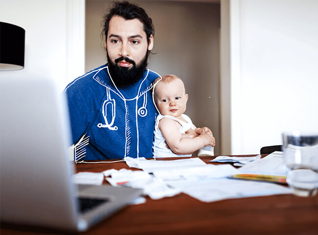 Junger Medizinstudent sitzt mit seinem Baby am Schreibtisch und lernt.
