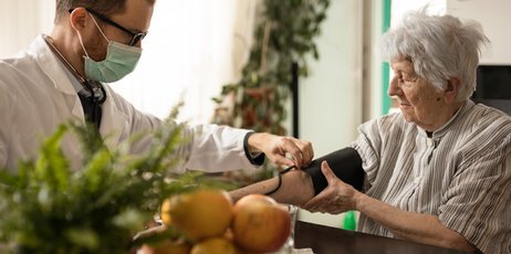 Arzt misst während eines Hausbesuches den Blutdruck einer Patientin. 