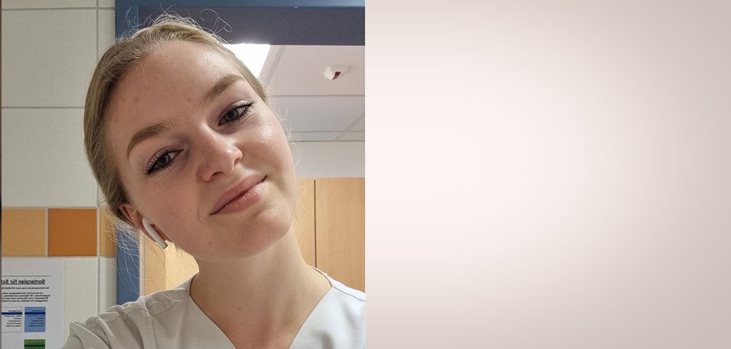Karolina trägt einen Kittel im Krankenhaus und lächelt in die Kamera. 