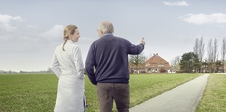 Ein Mann spricht mit einer Frau in einem weißen Kittel, während sie auf dem Land spazieren