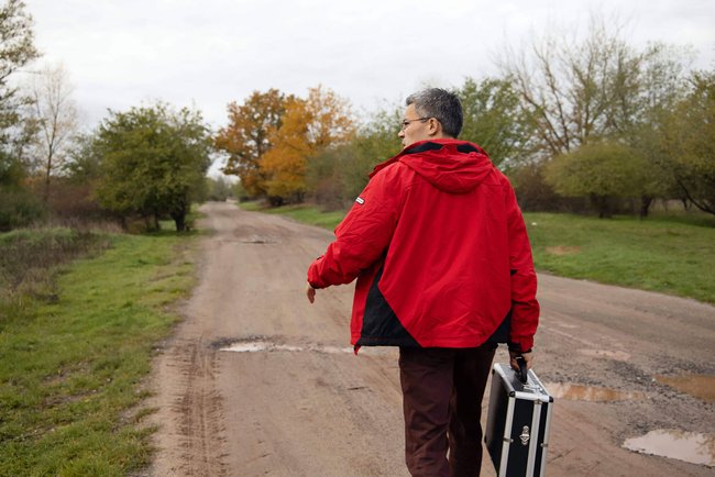 Der Landarzt Charles Schupet geht in einem Dorf mit seinem Arztkoffer über einen Feldweg.