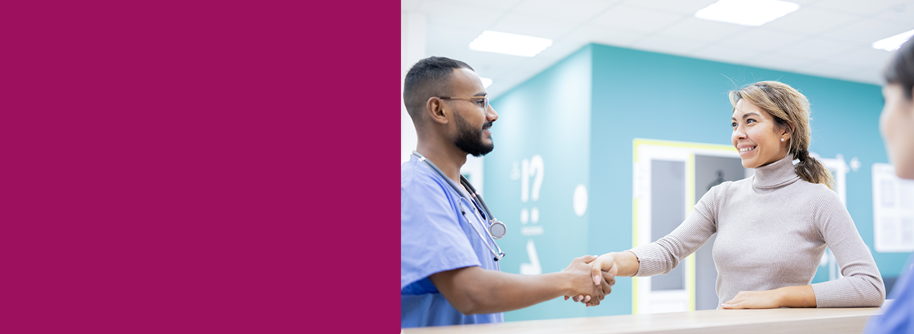 Ein niedergelassener Arzt begrüßt in einer Praxis am Empfangstresen eine junge Patientin.