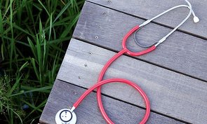 Auf einem Holzsteg liegt ein rotes Stethoskop. 