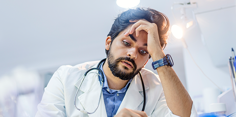 Ein übermüdeter Arzt sitzt während seiner Schicht am Schreibtisch.