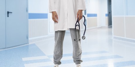 Ein Arzt in einem Krankenhaus der Jogginghose und Kittel trägt und ein Stethoskop in der Hand hält