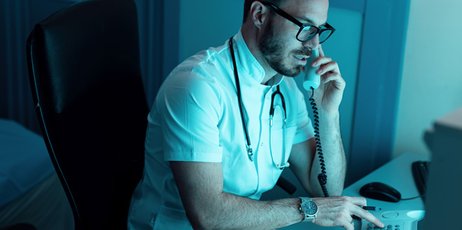 Männlicher Arzt telefoniert am Schreibtisch während der Nachtschicht. 