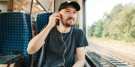 Ein Mann sitzt in einem Zug und blickt auf die vorbeiziehende Landschaft.