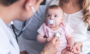 Ein Kinderarzt untersucht ein Baby, das ihn aufmerksam beobachtet.