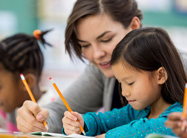 Eine Ärztin hilft Grundschulkindern beim Schreiben lernen.
