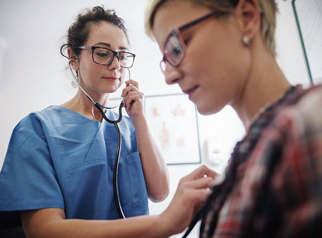 Junge Medizinstudentin hört Patientin mit Stethoskop ab.