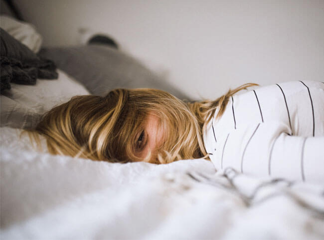 Medizinstudentin liegt unmotiviert und mit Haaren über dem Gesicht im Bett
