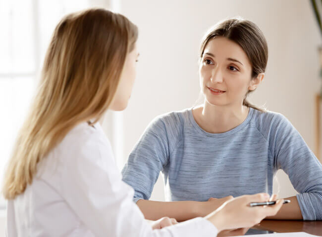 Eine junge Patientin wird von ihrer Ärztin in einem vertraulichen Gespräch über Risiken ihrer Behandlung aufgeklärt.