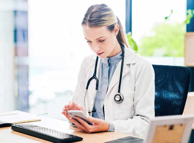 Eine Ärztin sitzt in ihrer Praxis und informiert sich an ihrem Handy über Medizin-News.