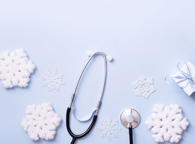 Ein Stethoskop liegt auf blauem Hintergrund. Zu sehen sind auch Wintermotive wie Schneeflocken und Geschenke. 