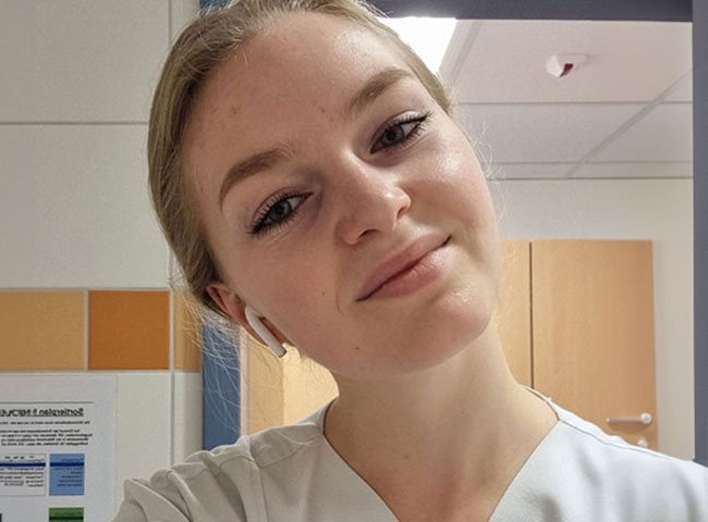 Karolina trägt einen Kittel im Krankenhaus und lächelt in die Kamera. 