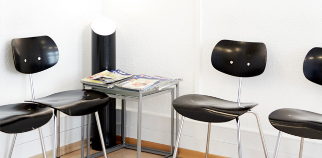 Ein weißer Raum mit vier Stühlen und einem Tisch mit Magazinen drauf.