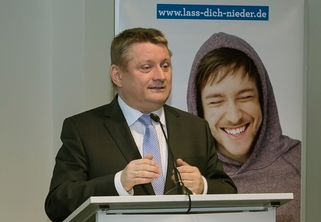 Bundesgesundheitsminister Hermann Gröhe steht am Pult, im Hintergrund ist ein Plakat