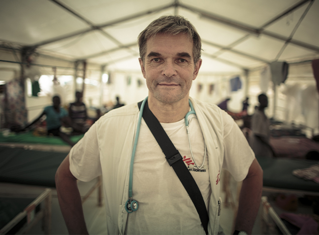 Dr. Klaus Volmer steht im Behandlungszelt eines Flüchtlingslagers im Südsudan und schaut in die Kamera. 