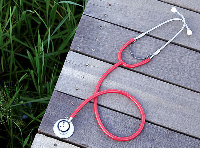 Auf einem Holzsteg liegt ein rotes Stethoskop. 