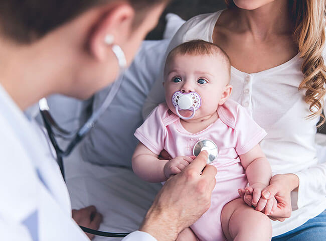 Ein Kinderarzt untersucht ein Baby, das ihn aufmerksam beobachtet.