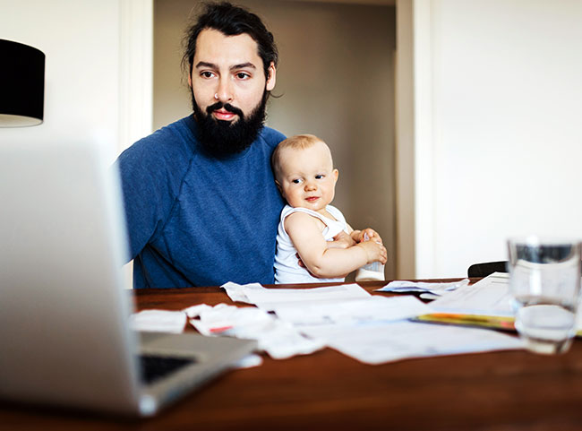 Ein Vater mit seinem Kind auf dem Schoß studiert am Laptop