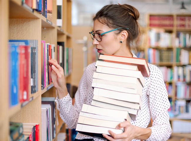 Frau in einer Bücherei mit vielen Büchern auf ihrem Arm