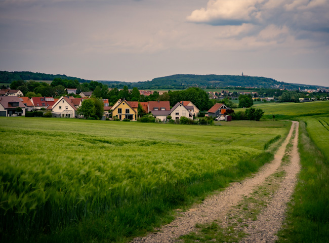 Ein Weg führt an grünen Feldern vorbei zu einem kleinen Dorf.